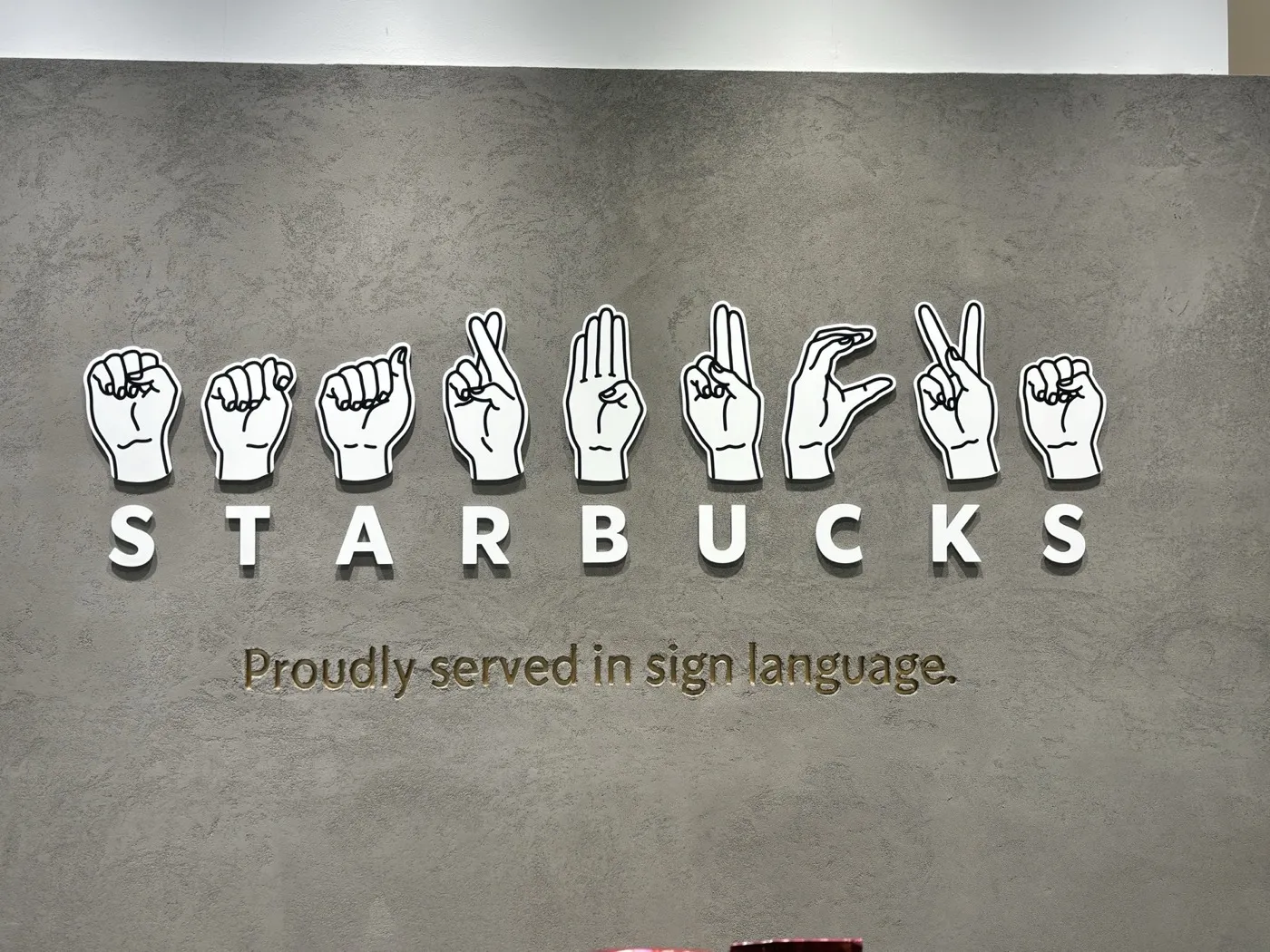 nonowa国立店の壁面サイン。指文字のSTARBUCKSとProudly served in sign languageの文字