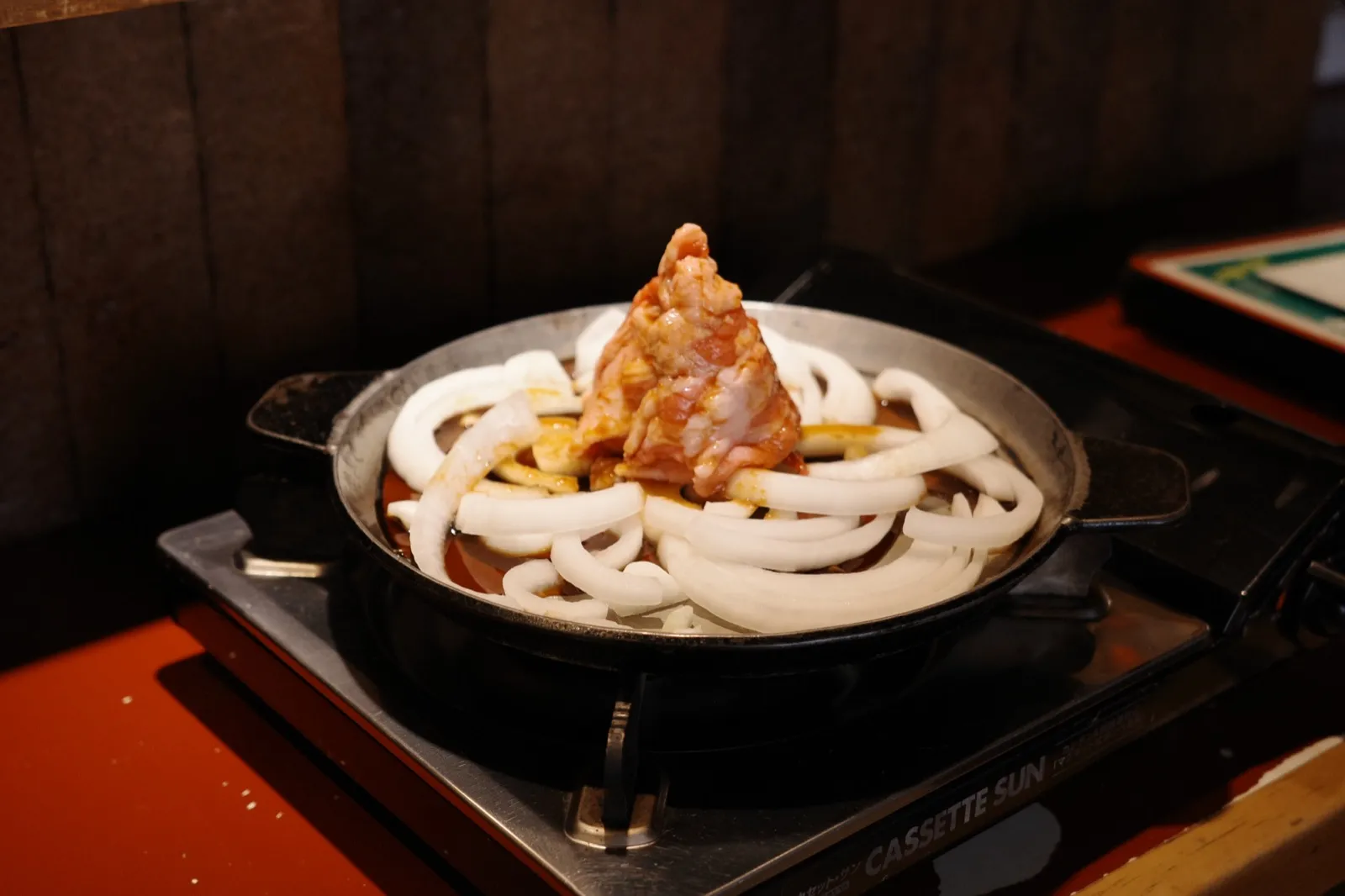 調理前の十和田バラ焼き。鉄鍋のたれと円状の玉ねぎ、中央に牛バラ肉