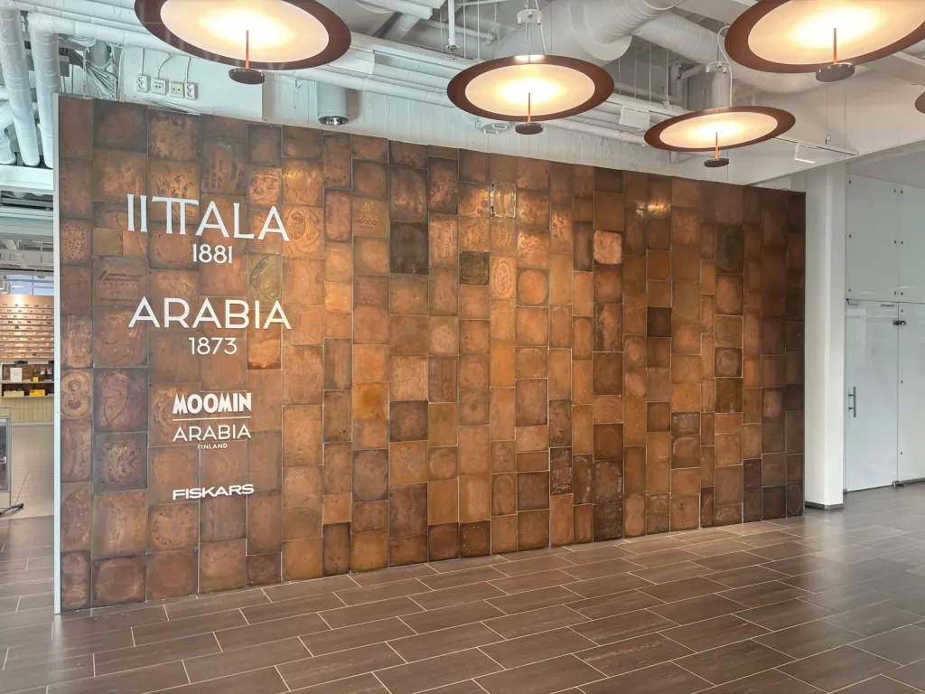 IITTALA 1881、ARABIA 1873、MOOMIN ARABIA、FISKARS のロゴが並ぶ銅板の壁